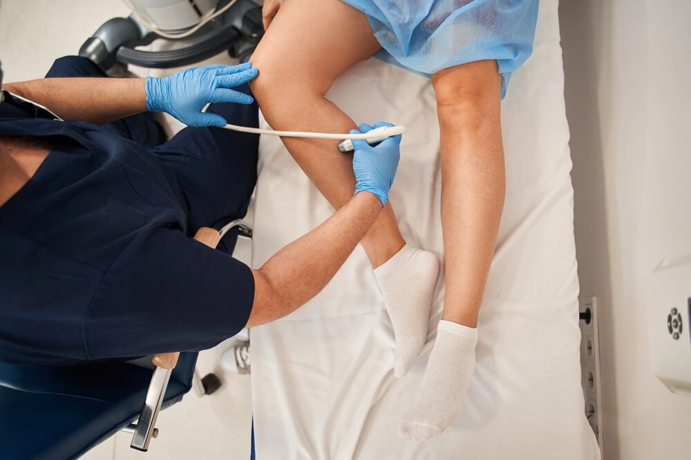Orthopedist doctor doing ultrasound examination of patient's leg veins in his office